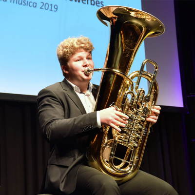 Tuba spielender Junge in Anzug auf der Bühne