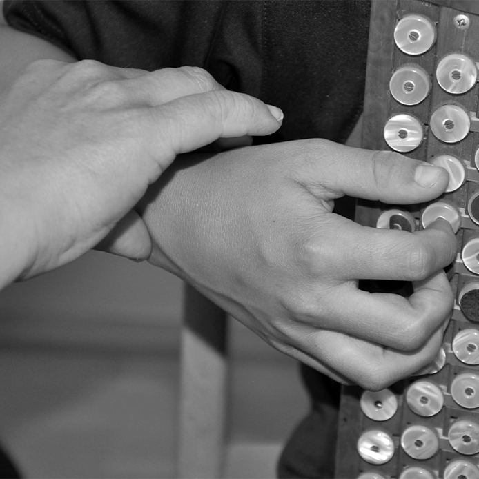 Lehrerhände fassen Handgelenk des Harmonika-spielenden Schülers sanft an