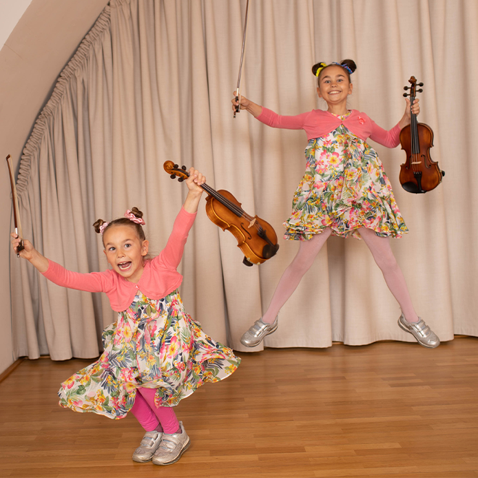 Foto zweier Mädchen, die mit Geige und Bogen in die Höhe springen