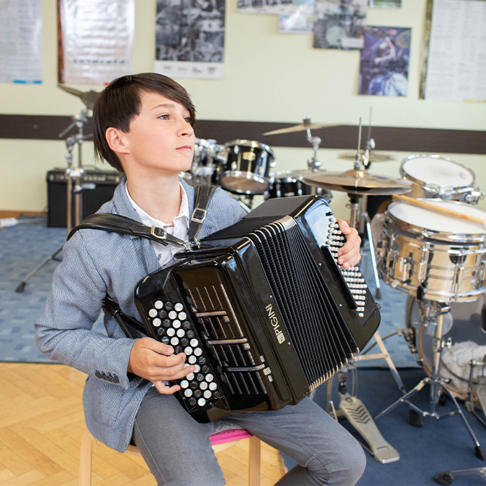 Junge beim Akkordeon spielen, im Hintergrund befindet sich ein Drumset