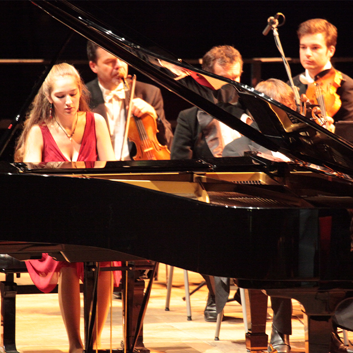 Pianistin am Konzertflügel vor einem Orchester