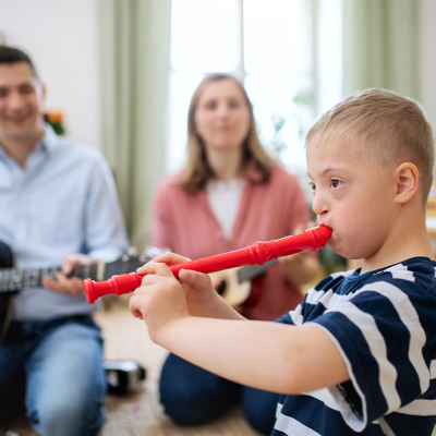 Junge mit Down-Syndrom beim Spielen auf einer roten Blockflöte