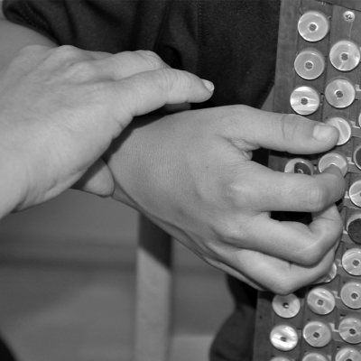 Lehrerhände fassen Handgelenk des Harmonika-spielenden Schülers sanft an