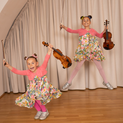 Foto zweier Mädchen, die mit Geige und Bogen in die Höhe springen