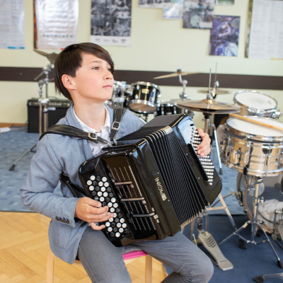 Junge beim Akkordeon spielen, im Hintergrund befindet sich ein Drumset