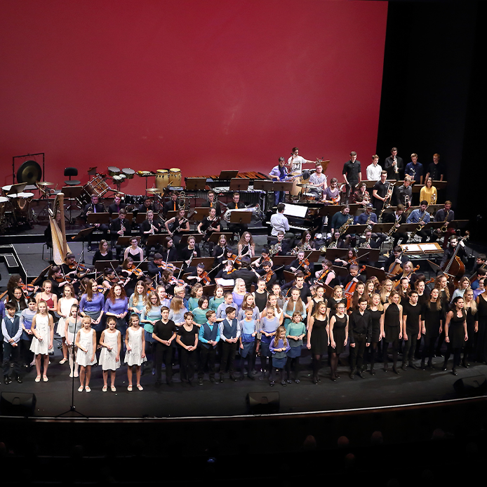 Bild einer Chor- und Orchesteraufführung mit vielen Kindern und Jugendlichen auf der Bühne, aus der Vogelperspektive fotografiert