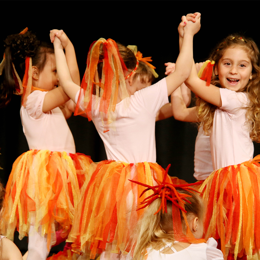 Mädchen in bunten Kostümen tanzend, sich an den Händen fassend, auf der Bühne
