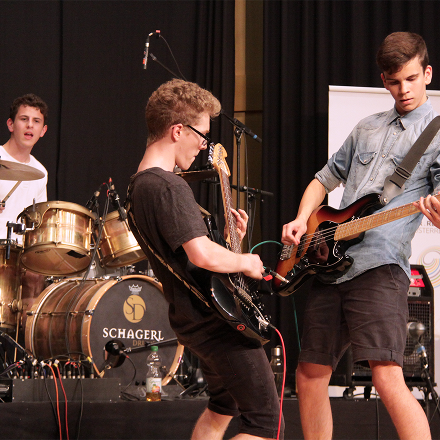 Eine Musikschul-Band, bestehend aus Bassist, Gitarrist und Drummer, beim Performen auf der Bühne