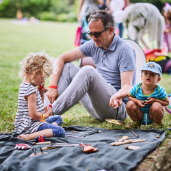 Vater mit zwei Kindern beim Ausprobieren von Orff-Instrumenten