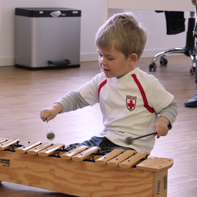Junge der sitzend auf dem Boden mit Schlägeln auf einem Xylophon spielt